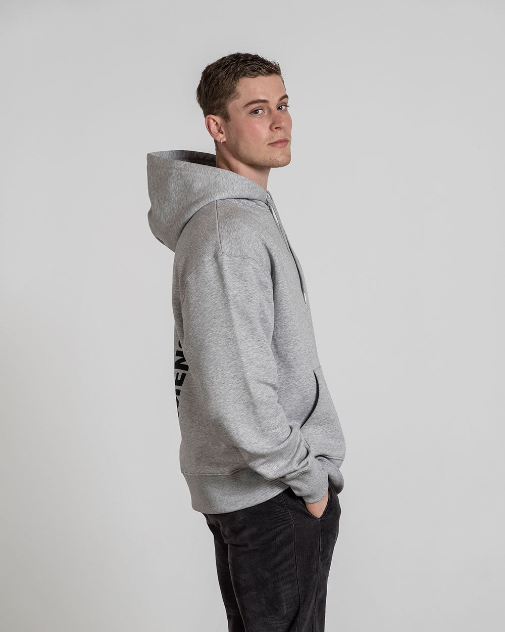 Grauer Hoodie mit aufgesetzter Kapuze in Profilansicht; Rückendruck „MENSCH“ leicht sichtbar an der Seite.