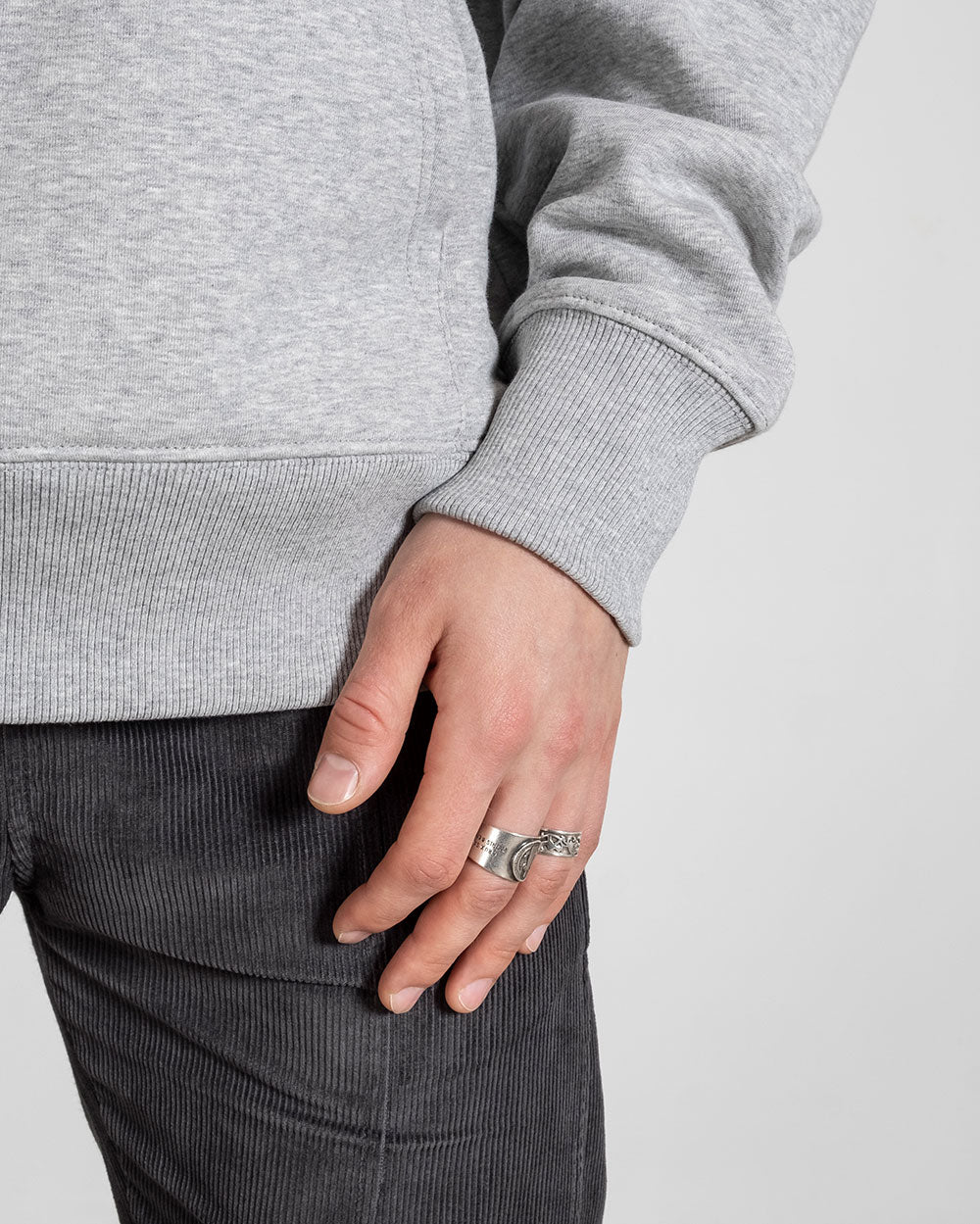 Nahaufnahme des Ärmels und Hüftbundes des grauen Hoodies; das Model trägt mehrere silberne Ringe an der linken Hand.