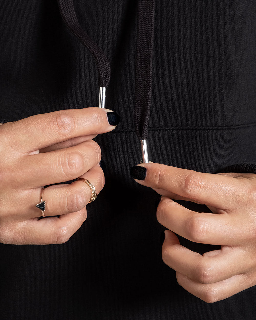 Nahaufnahme der beiden schwarzen Hoodie-Kordeln mit silberfarbenen Endstücken, gehalten zwischen den Fingern.