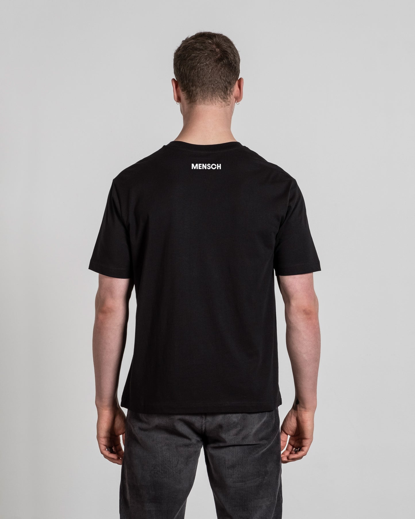 Schwarzes T-Shirt mit weißem „MENSCH“-Schriftzug im Nackenbereich, von hinten gezeigt.