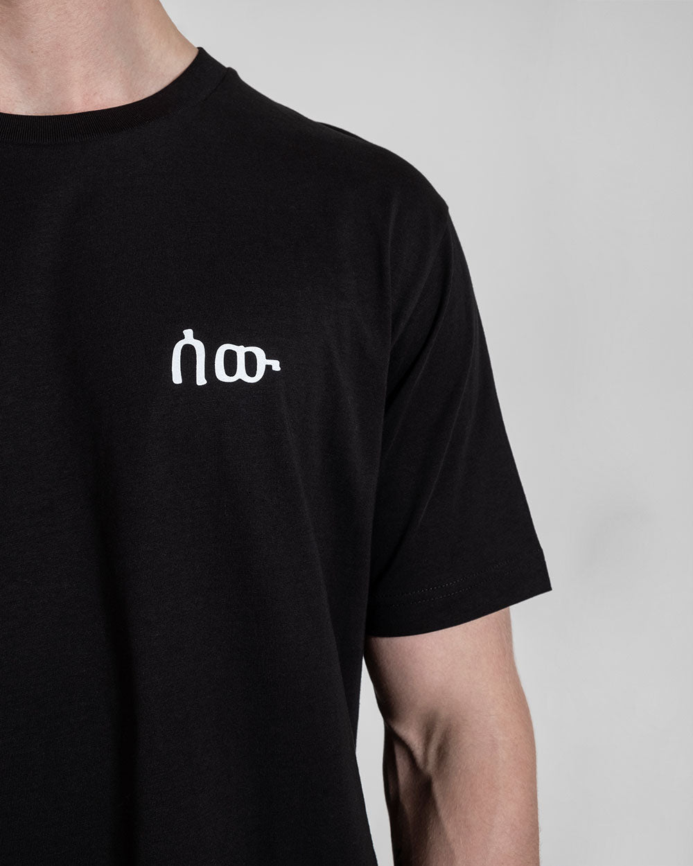 Detailaufnahme des weißen Logos auf der linken Brust eines schwarzen T-Shirts.