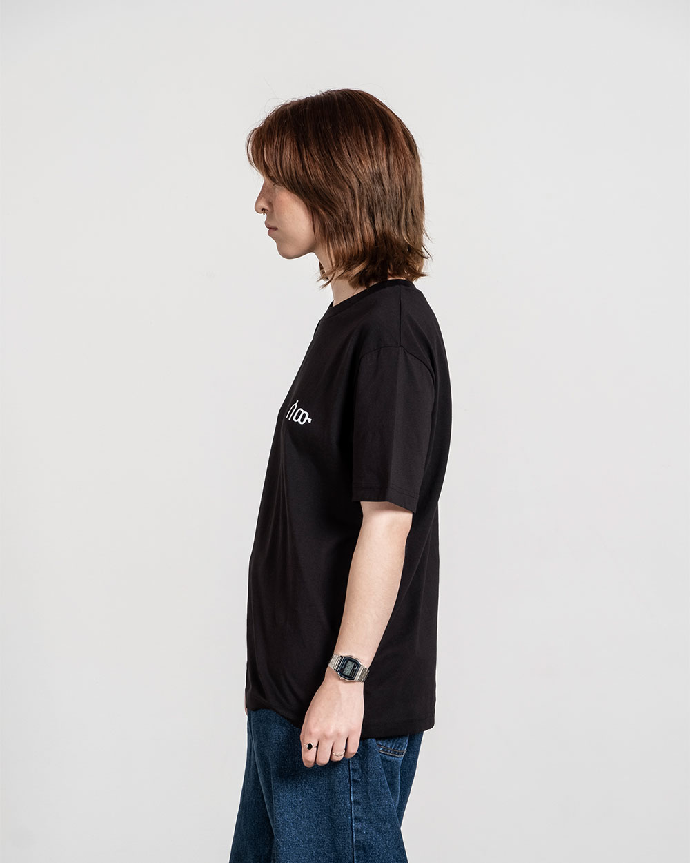 Schwarzes T-Shirt mit weißem Brustlogo, seitlich getragen gezeigt.