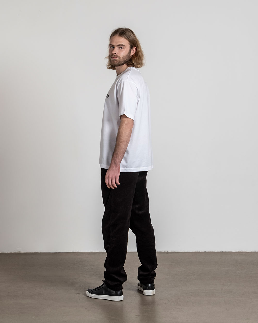 Weißes T-Shirt mit Frontprint, seitliche Ansicht eines stehenden Models mit Blick zur Kamera.