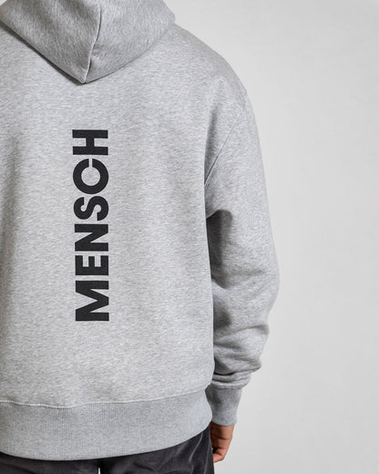 Nahaufnahme des vertikalen Rückendrucks „MENSCH“ in Schwarz auf grauem Sweatstoff, Kapuze leicht sichtbar von hinten.