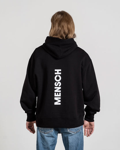 Rückansicht des schwarzen Hoodies mit vertikalem weißen „MENSCH“-Schriftzug, getragen von einer Person mit mittellangem Haar.