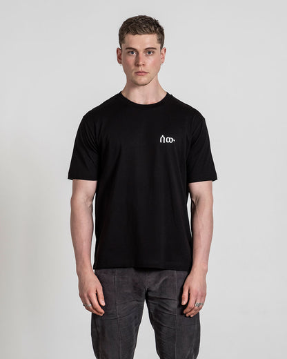 Schwarzes T-Shirt mit weißem Logo auf der linken Brust, frontal getragen fotografiert.