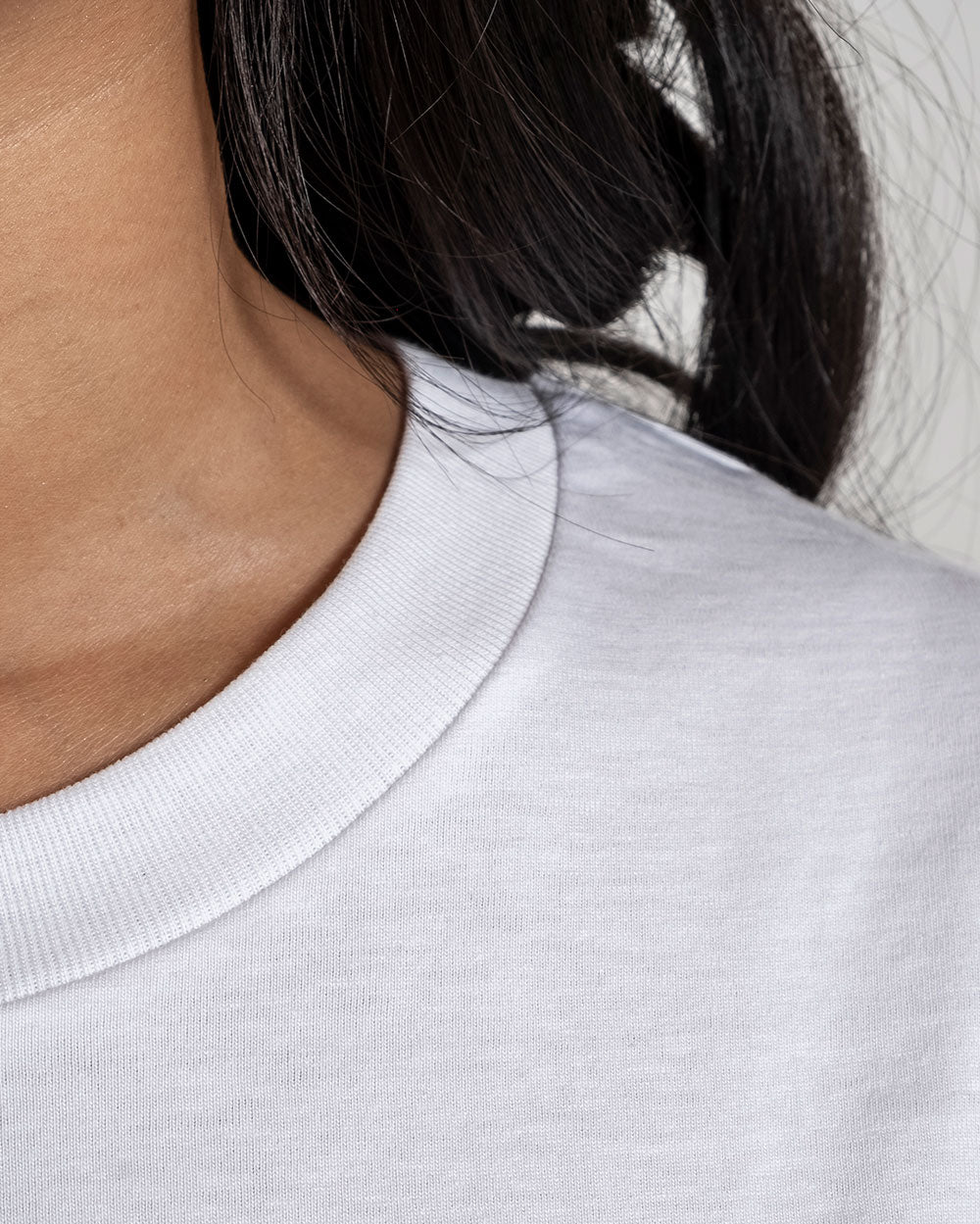  Detailansicht des weißen Rundhalsausschnitts eines T-Shirts, Fokus auf die feine Struktur des Stoffes und die Verarbeitung.
